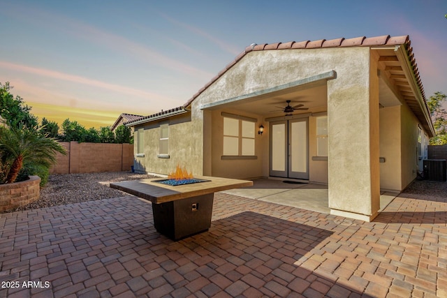 patio terrace at dusk featuring ceiling fan, central air condition unit, french doors, and a fire pit