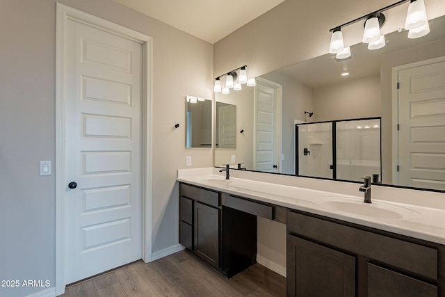 full bath featuring a shower stall, wood finished floors, double vanity, and a sink