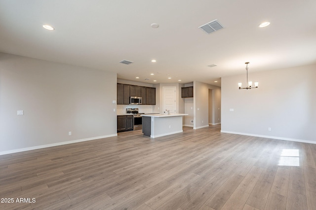unfurnished living room featuring visible vents, light wood finished floors, and an inviting chandelier