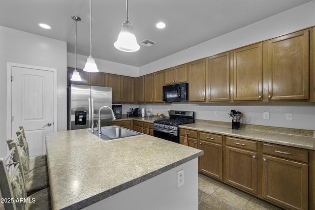 kitchen with hanging light fixtures, appliances with stainless steel finishes, a sink, an island with sink, and visible vents
