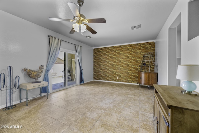 interior space featuring baseboards, ceiling fan, brick wall, and visible vents