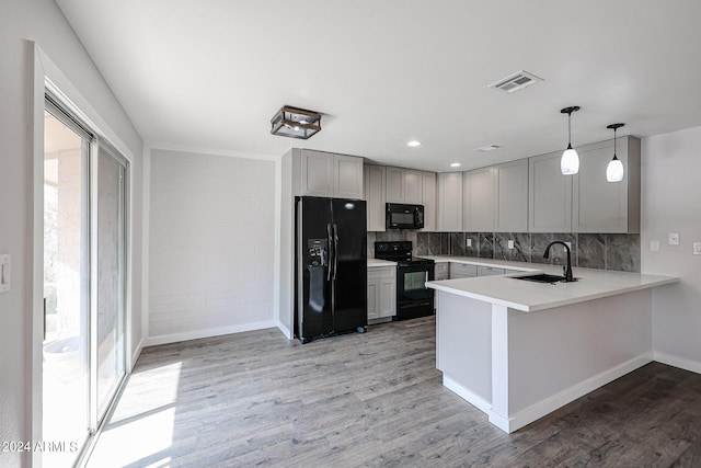 kitchen featuring a peninsula, a sink, hanging light fixtures, light countertops, and black appliances