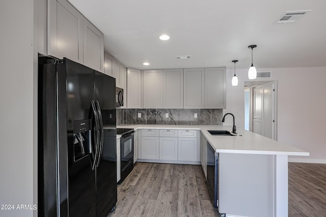 kitchen with a peninsula, a sink, light countertops, black appliances, and pendant lighting