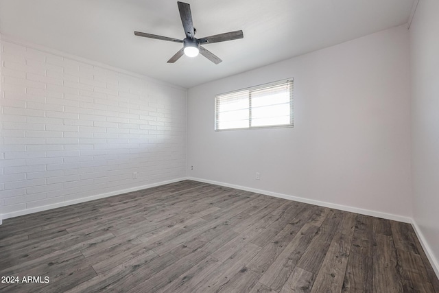 unfurnished room featuring a ceiling fan, brick wall, baseboards, and dark wood-style flooring