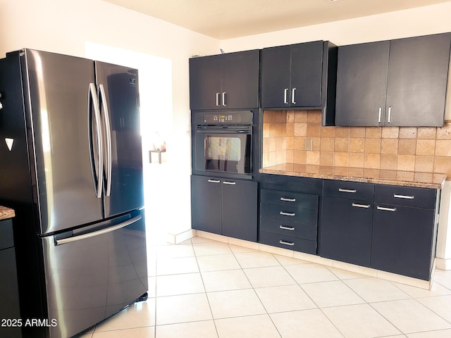 kitchen with backsplash, stainless steel refrigerator, light stone counters, and black oven