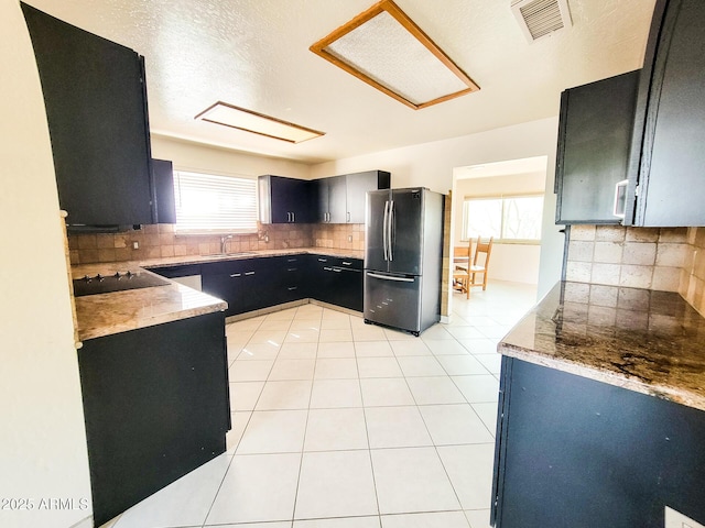 kitchen featuring black electric stovetop, light tile patterned floors, sink, backsplash, and stainless steel fridge