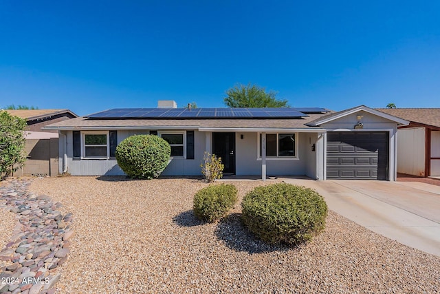 ranch-style house featuring a garage, roof mounted solar panels, and concrete driveway