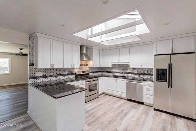 kitchen with sink, light hardwood / wood-style flooring, wall chimney exhaust hood, ceiling fan, and stainless steel appliances