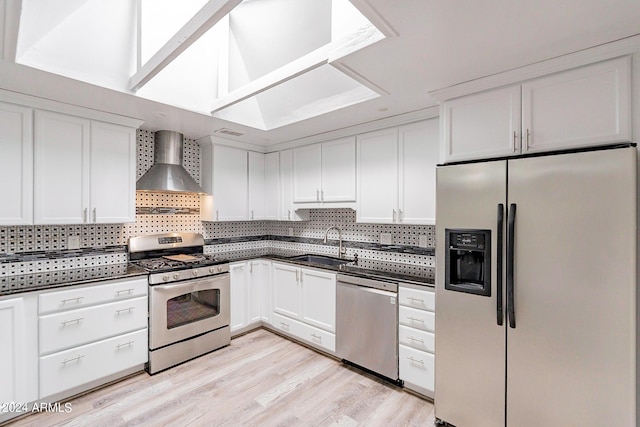 kitchen with dark countertops, a sink, stainless steel appliances, wall chimney range hood, and backsplash