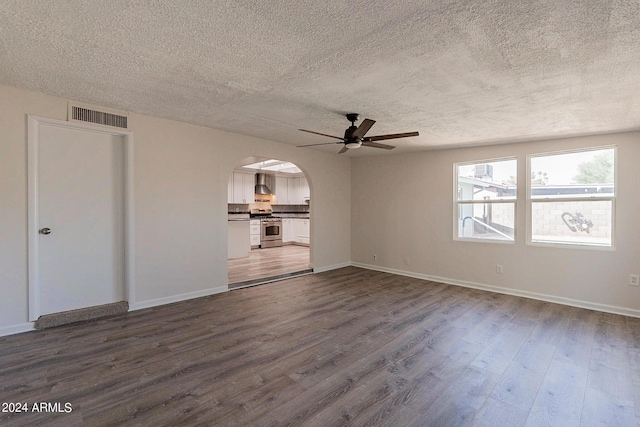 unfurnished living room with arched walkways, dark wood finished floors, visible vents, and baseboards