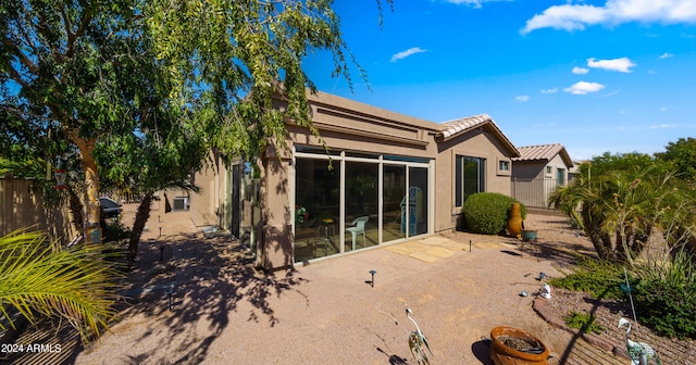 rear view of house featuring stucco siding, a tile roof, fence, and a patio