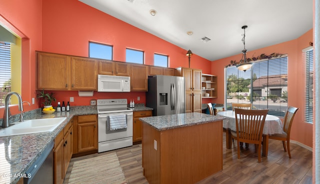 kitchen with a center island, decorative light fixtures, appliances with stainless steel finishes, a sink, and light stone countertops