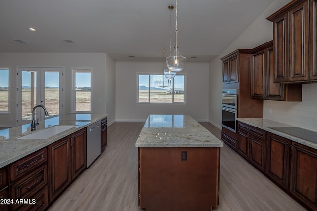 kitchen with sink, decorative light fixtures, a kitchen island, stainless steel appliances, and light stone countertops