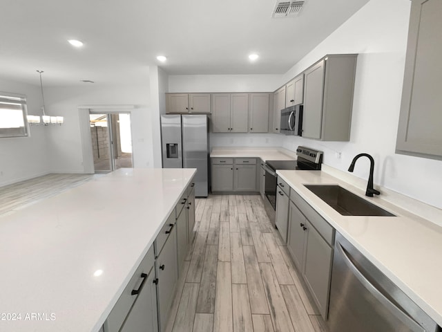 kitchen featuring light wood-type flooring, sink, hanging light fixtures, gray cabinetry, and stainless steel appliances