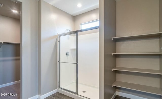 bathroom featuring a spacious closet, a stall shower, and baseboards