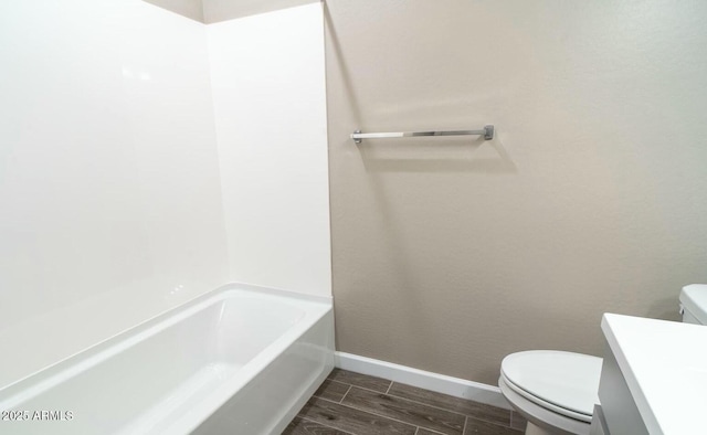 bathroom with a tub to relax in, baseboards, toilet, vanity, and wood finish floors