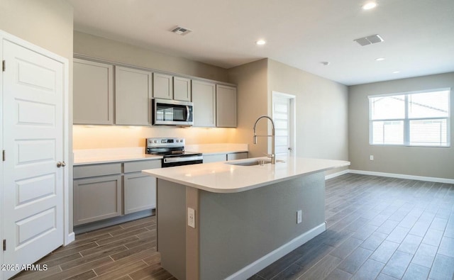 kitchen with stainless steel appliances, gray cabinetry, a sink, and a center island with sink