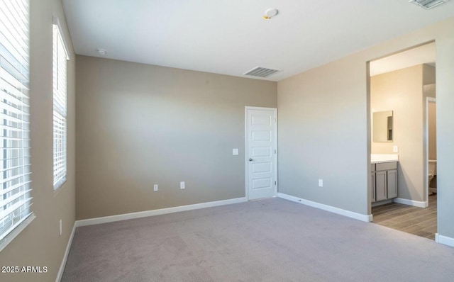 unfurnished bedroom featuring light carpet, ensuite bathroom, visible vents, and baseboards