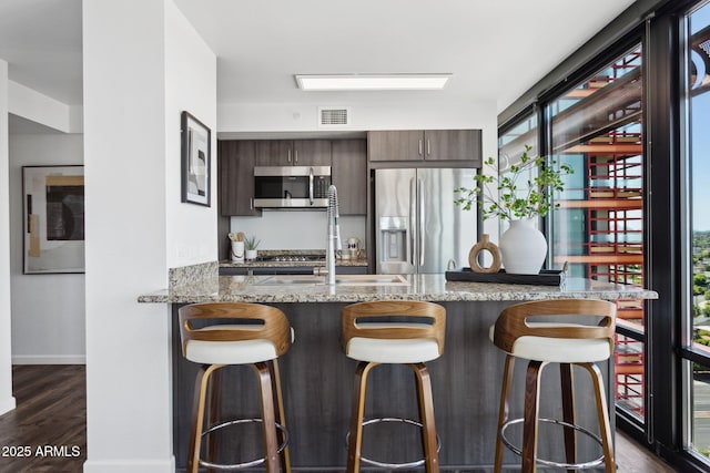 4808 N 24th St Unit 1228, Phoenix, AZ 85016 - kitchen featuring appliances with stainless steel finishes, dark wood-type flooring, a kitchen breakfast bar, light stone countertops, and a peninsula