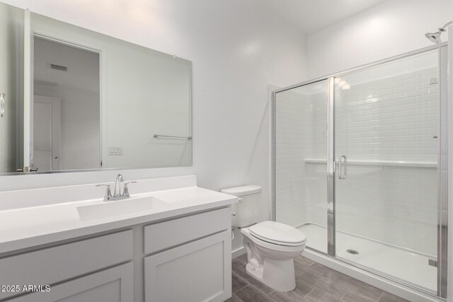 bathroom with wood finished floors, visible vents, toilet, vanity, and a stall shower