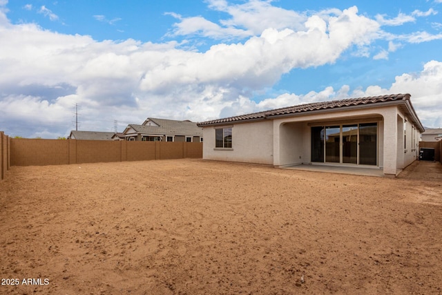 back of house featuring a fenced backyard, a tiled roof, and stucco siding