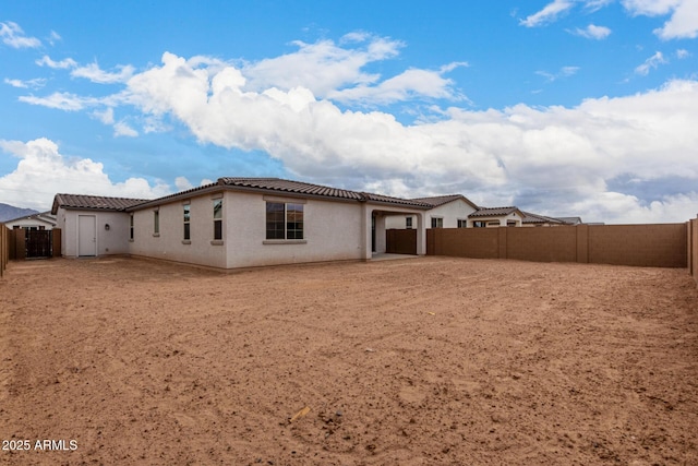 back of house with a fenced backyard, an attached garage, a tiled roof, and stucco siding