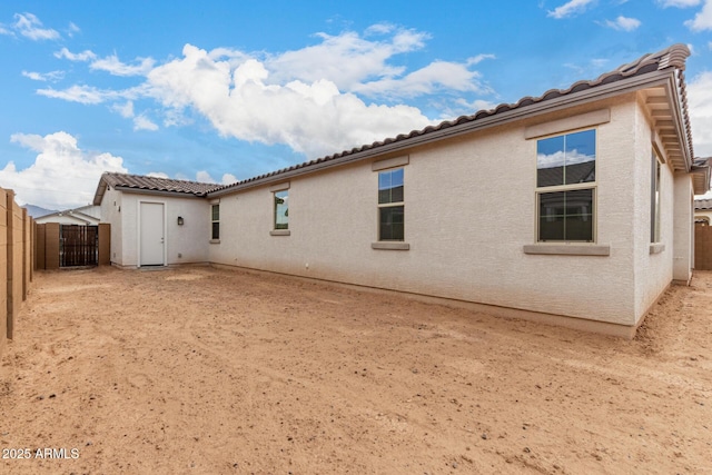 rear view of house with a fenced backyard, a tile roof, and stucco siding