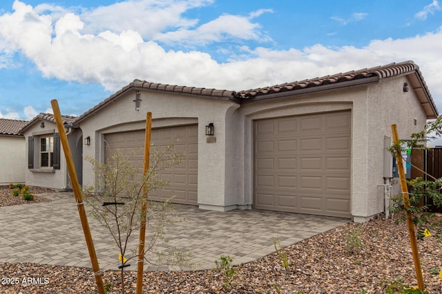 view of front facade featuring a garage, a tile roof, stucco siding, and decorative driveway