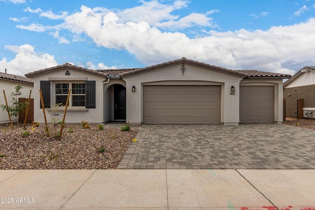 view of front of house featuring a garage, stucco siding, a tiled roof, and decorative driveway