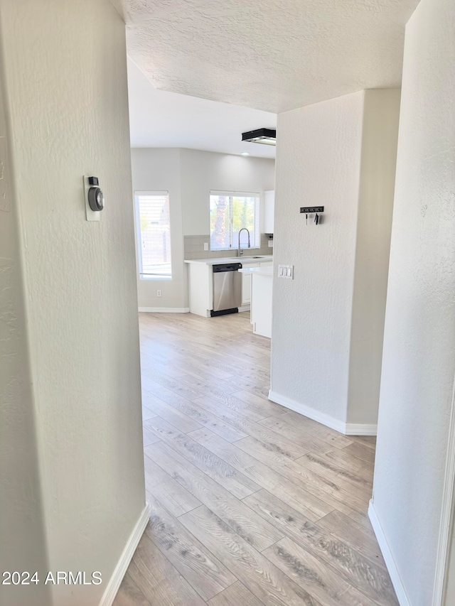 hallway with a textured ceiling, sink, and light wood-type flooring