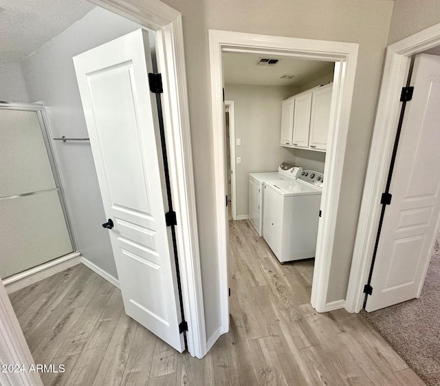 clothes washing area featuring light hardwood / wood-style floors, cabinets, and washer and dryer