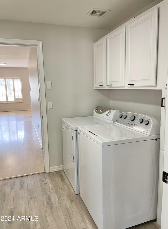 laundry area featuring cabinets, light hardwood / wood-style flooring, and washing machine and dryer