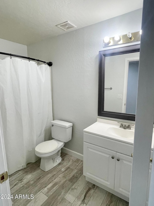 bathroom with hardwood / wood-style floors, a textured ceiling, walk in shower, toilet, and vanity