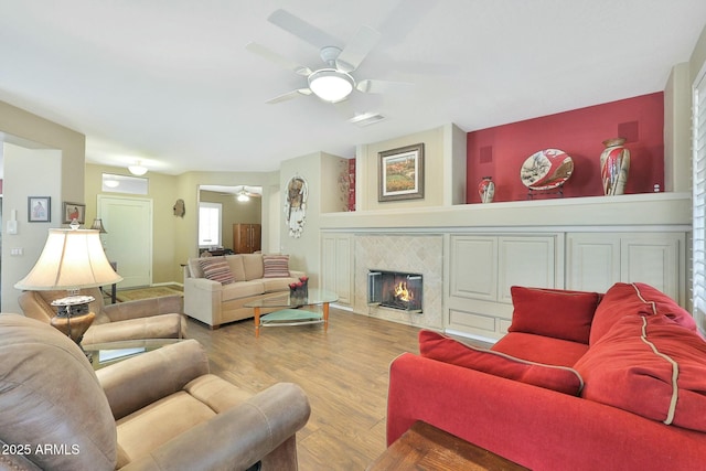 living area featuring a ceiling fan, visible vents, a fireplace, and wood finished floors