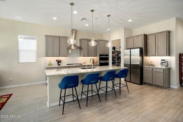 kitchen featuring sink, hanging light fixtures, wall chimney range hood, a kitchen bar, and appliances with stainless steel finishes