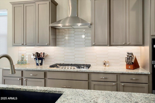 kitchen featuring tasteful backsplash, light stone countertops, wall chimney exhaust hood, and stainless steel gas cooktop