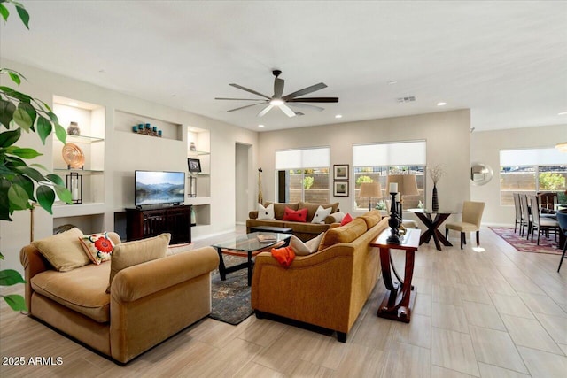 living room featuring built in shelves, ceiling fan, and a wealth of natural light