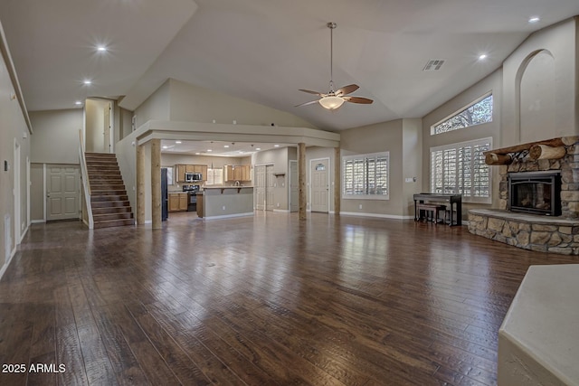 unfurnished living room featuring dark wood-type flooring, ceiling fan, a stone fireplace, and high vaulted ceiling