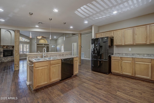 kitchen with a stone fireplace, sink, decorative light fixtures, a kitchen island with sink, and black appliances