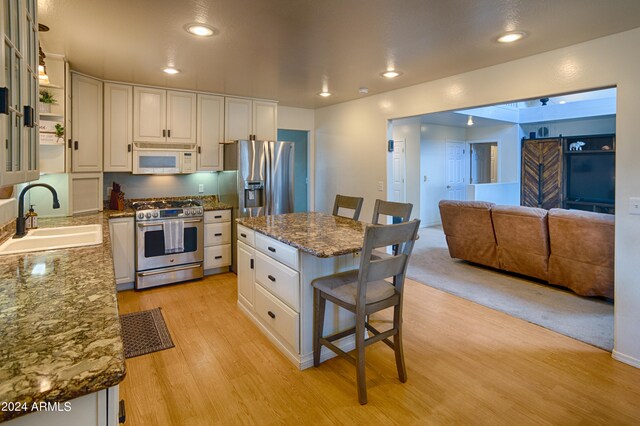 kitchen with a kitchen breakfast bar, light hardwood / wood-style floors, appliances with stainless steel finishes, white cabinets, and sink