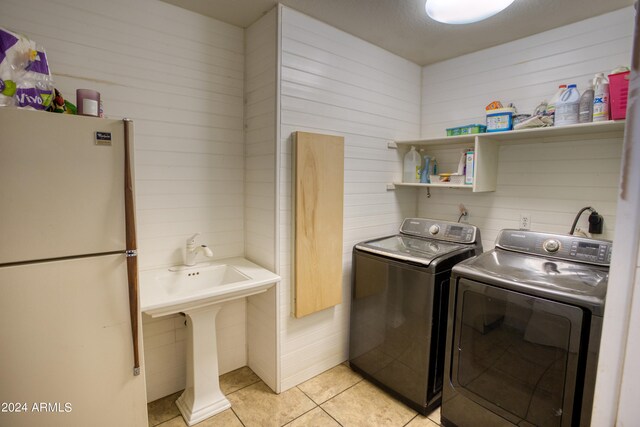 laundry room featuring washing machine and clothes dryer, light tile flooring, wooden walls, and hookup for an electric dryer