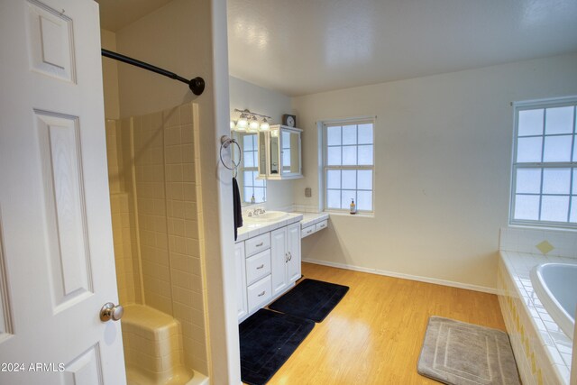 bathroom with hardwood / wood-style floors, vanity, and a relaxing tiled bath