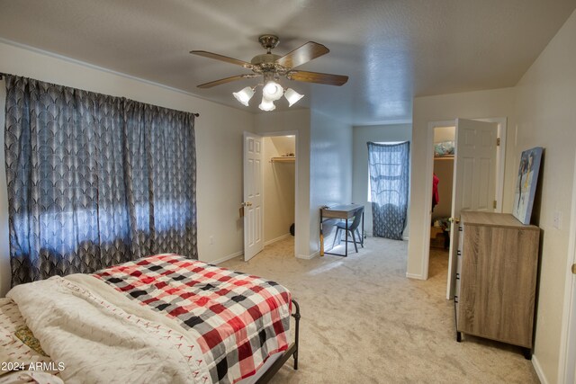 bedroom with light carpet, a closet, a walk in closet, and ceiling fan