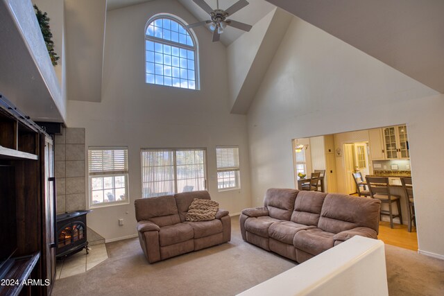 living room featuring high vaulted ceiling, ceiling fan, a wood stove, and light colored carpet