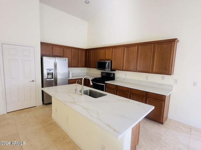 kitchen with sink, appliances with stainless steel finishes, high vaulted ceiling, light stone countertops, and an island with sink