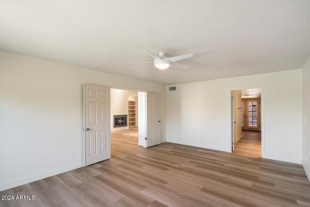 empty room with a textured ceiling, light hardwood / wood-style floors, built in features, and ceiling fan