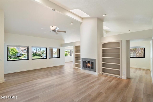 unfurnished living room with a skylight, ceiling fan, built in features, beam ceiling, and light hardwood / wood-style floors