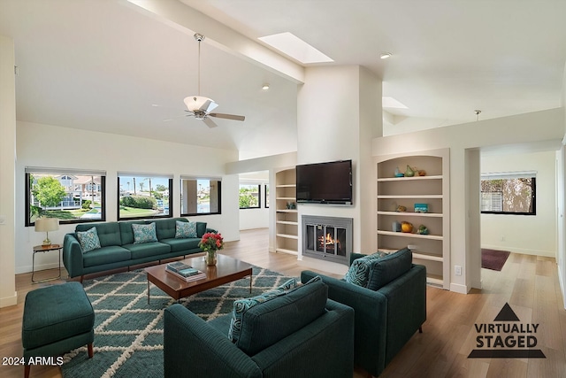 living room featuring built in shelves, ceiling fan, a skylight, beamed ceiling, and light hardwood / wood-style floors