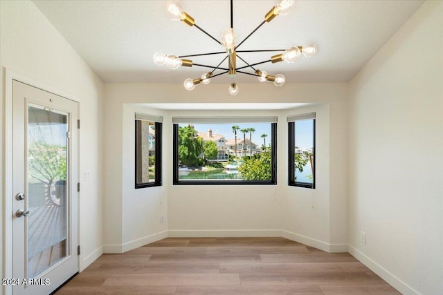 unfurnished dining area with a textured ceiling, light wood-type flooring, an inviting chandelier, and a healthy amount of sunlight