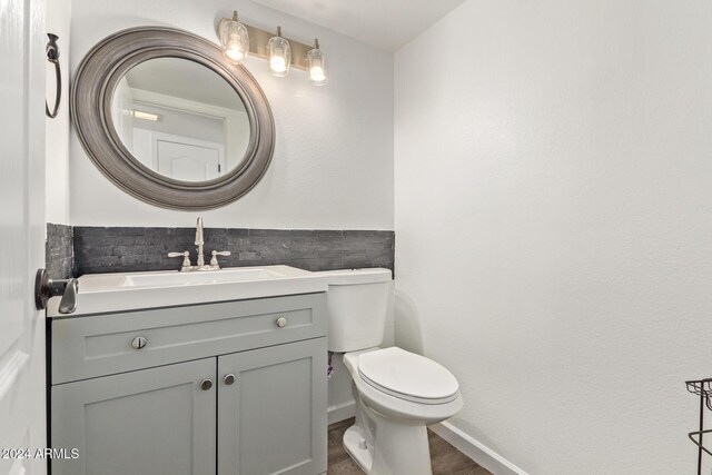 half bathroom featuring vanity, baseboards, toilet, and wood finished floors